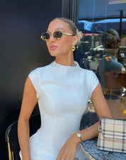 Woman wearing gold-rimmed sunglasses with white top and purse