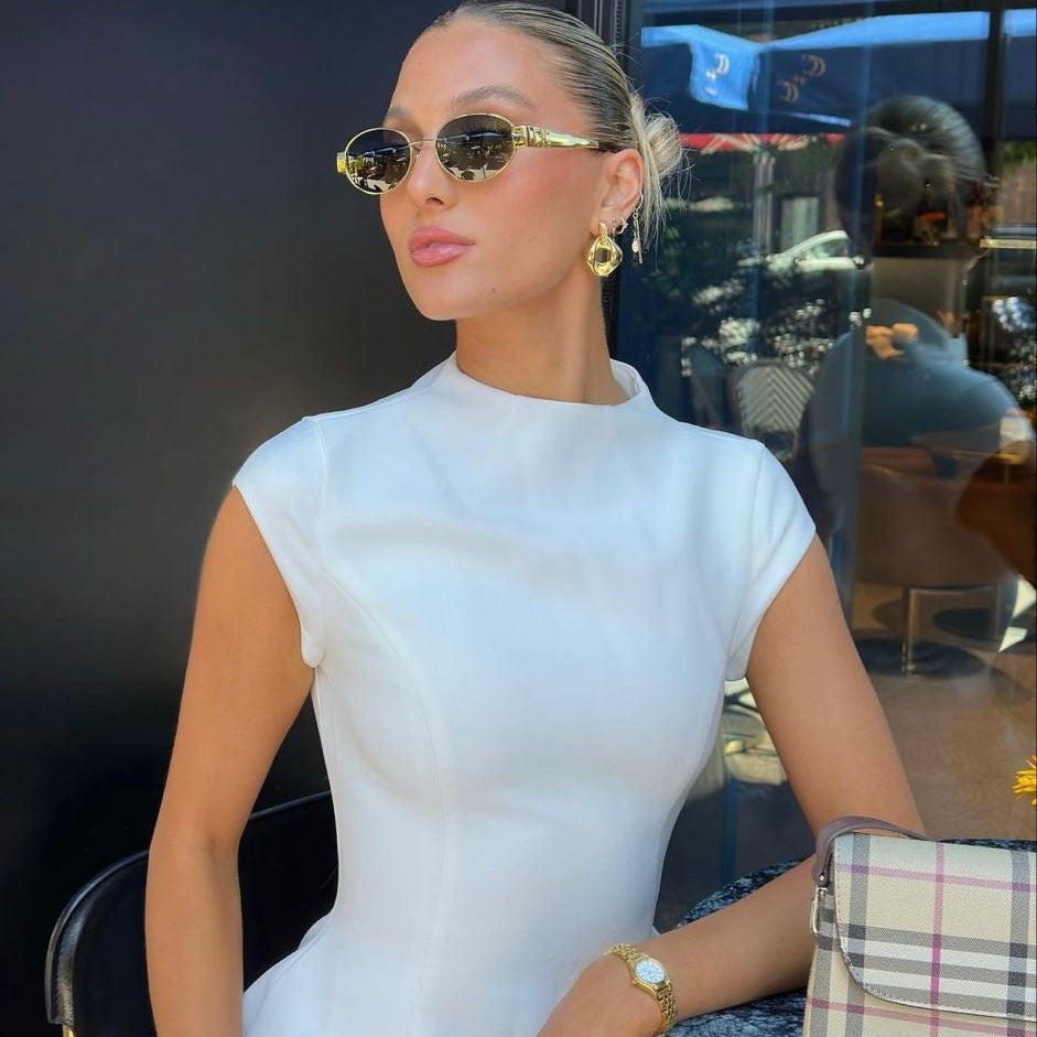Woman wearing gold-rimmed sunglasses with white top and purse