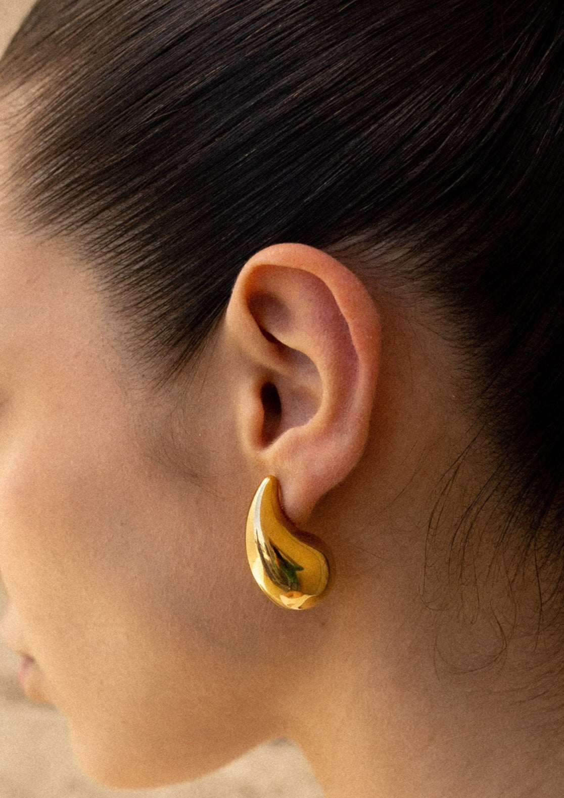Gold teardrop earrings on model, close-up ear detail