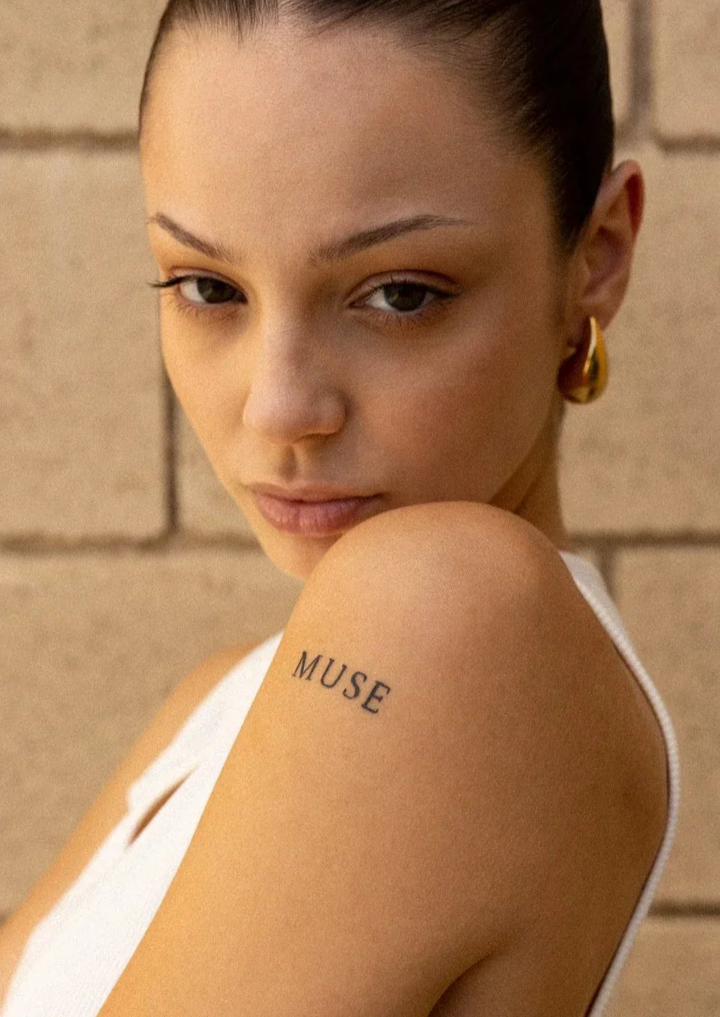 Gold teardrop earrings on model, front view with tattoo