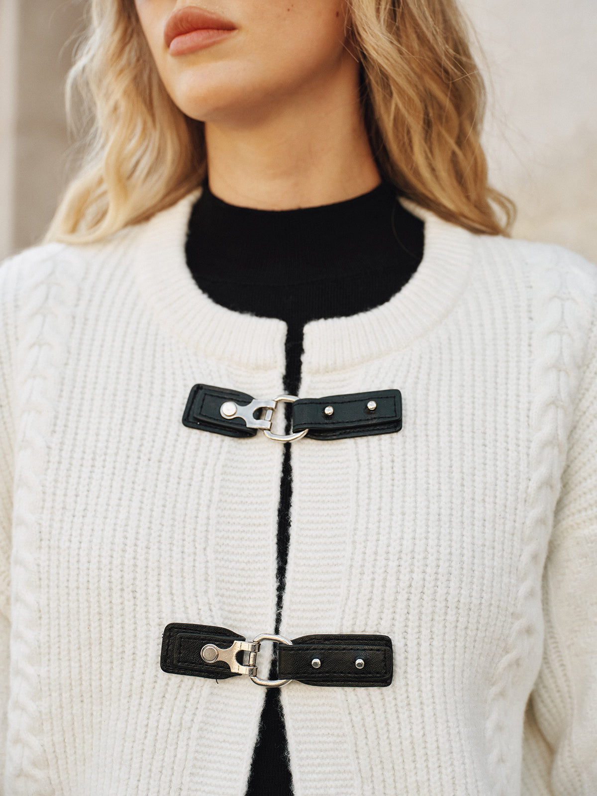Close-up of black buckle closures on cream knit vest