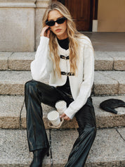 Cream knit vest with black buckle closures worn with black pants