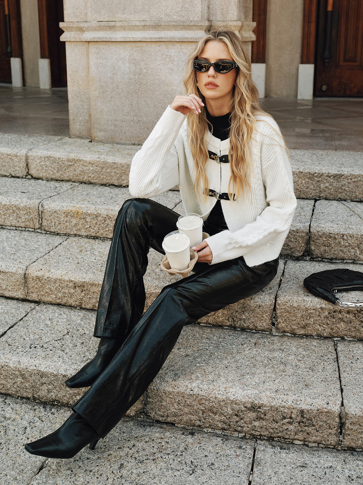 Cream knit vest with black buckle closures worn with black pants and boots