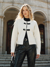 Cream knit vest with black buckle closures worn with black pants and belt