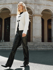 Cream knit vest with black buckle closures worn with black pants and boots, walking pose