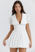 White mini dress with V-neck and pleated skirt front view with hands on hips