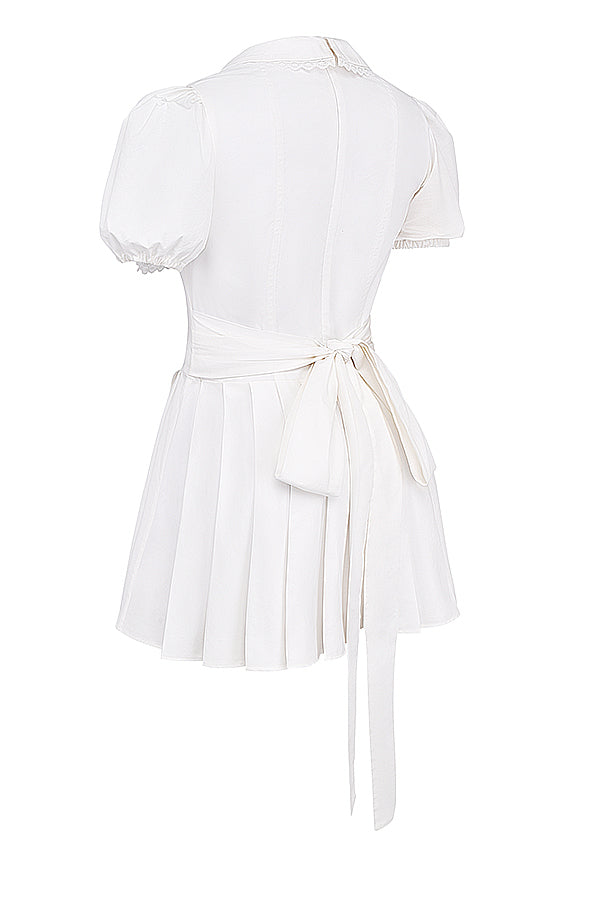 White mini dress with V-neck and pleated skirt isolated side view