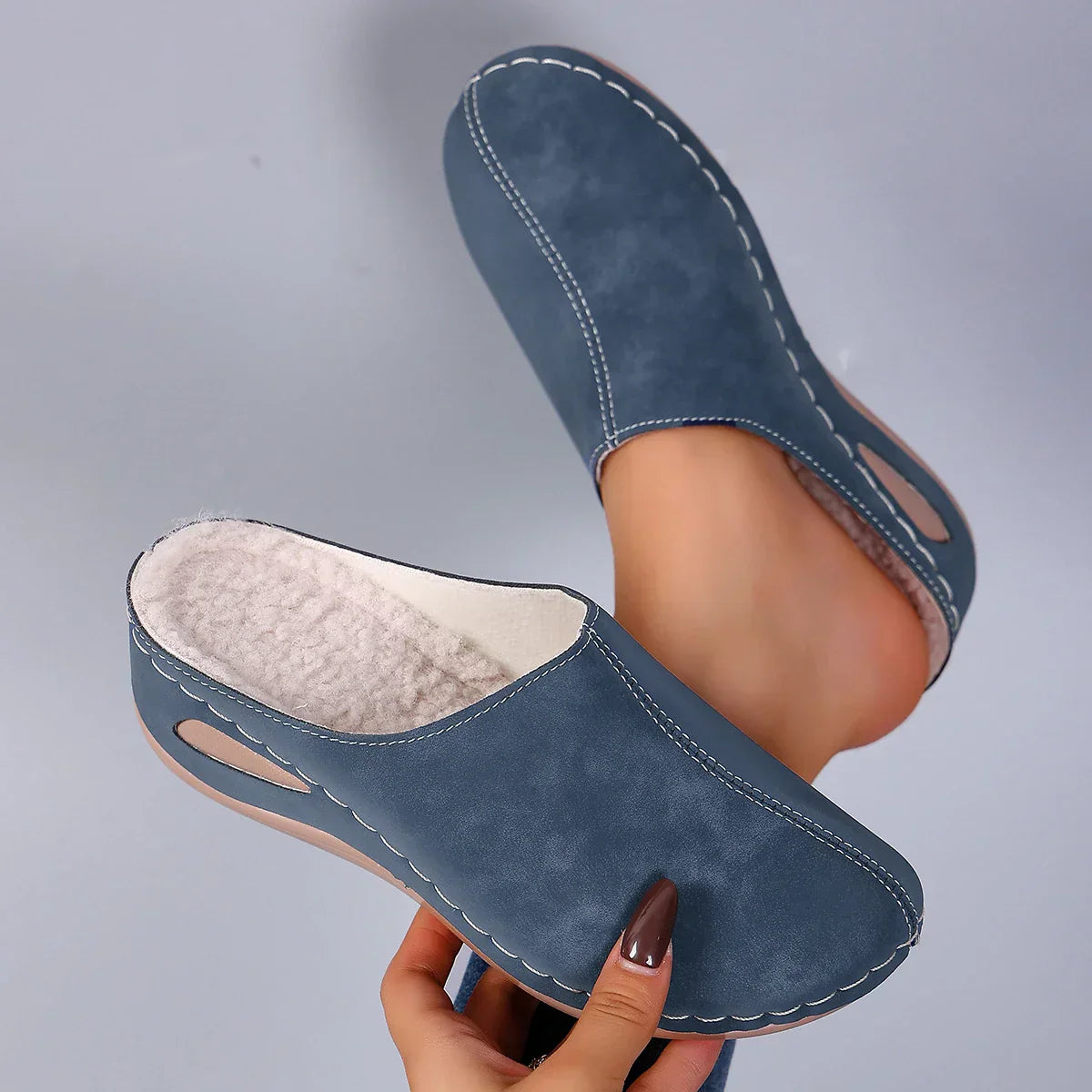 Blue suede slippers with white stitching and plush lining, front view