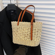 Woven straw tote bag with brown leather handles, front view with black blazer