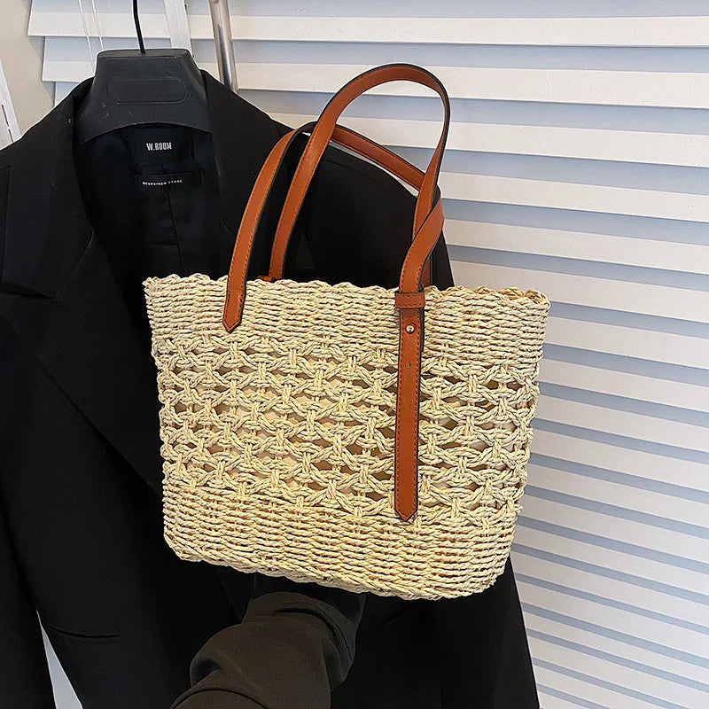 Woven straw tote bag with brown leather handles, front view with black blazer
