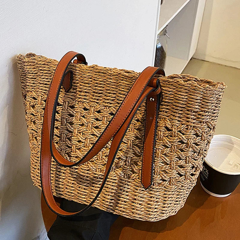 Woven straw tote bag with brown leather handles, side view on table