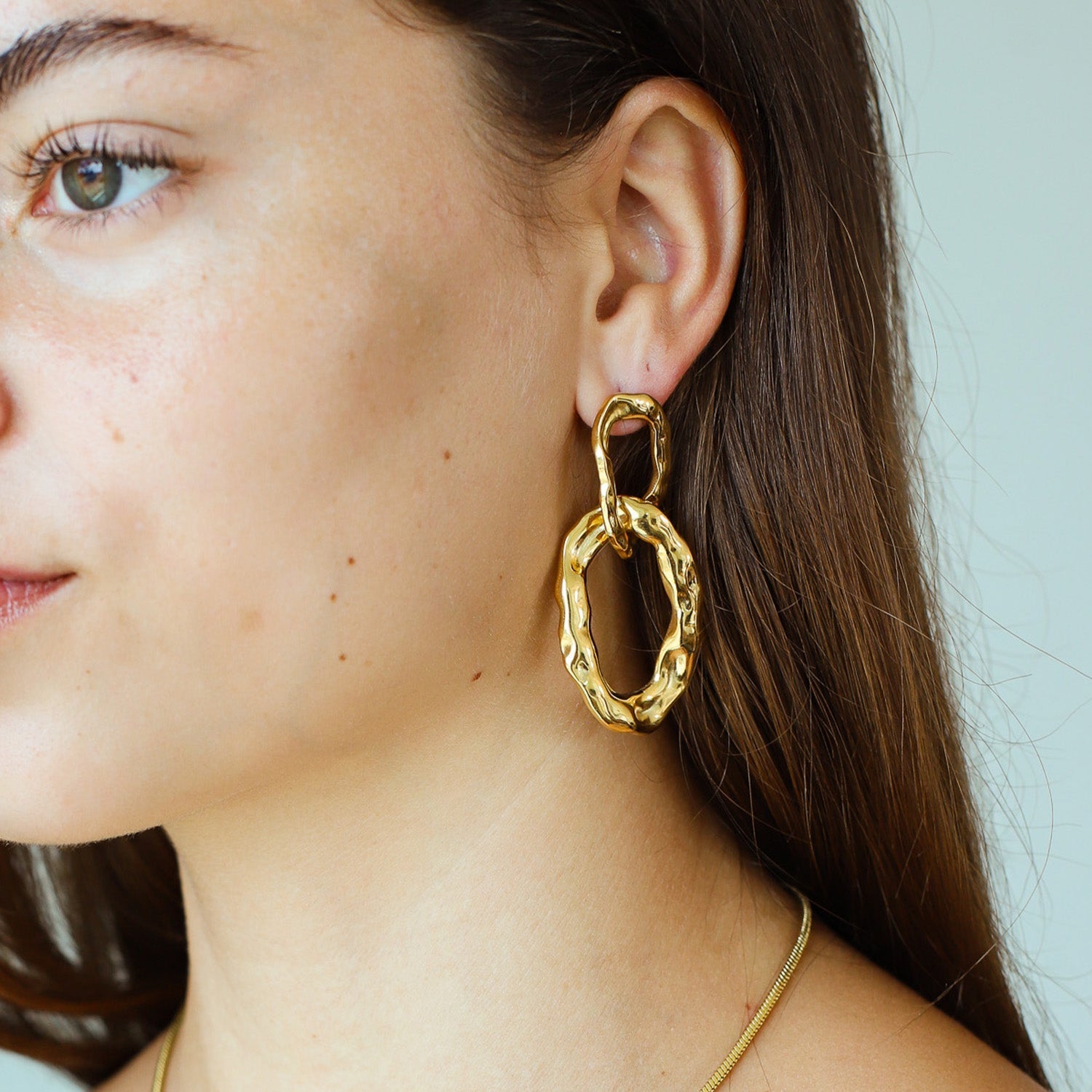 Gold-plated double-link hoop earrings worn on ear close-up