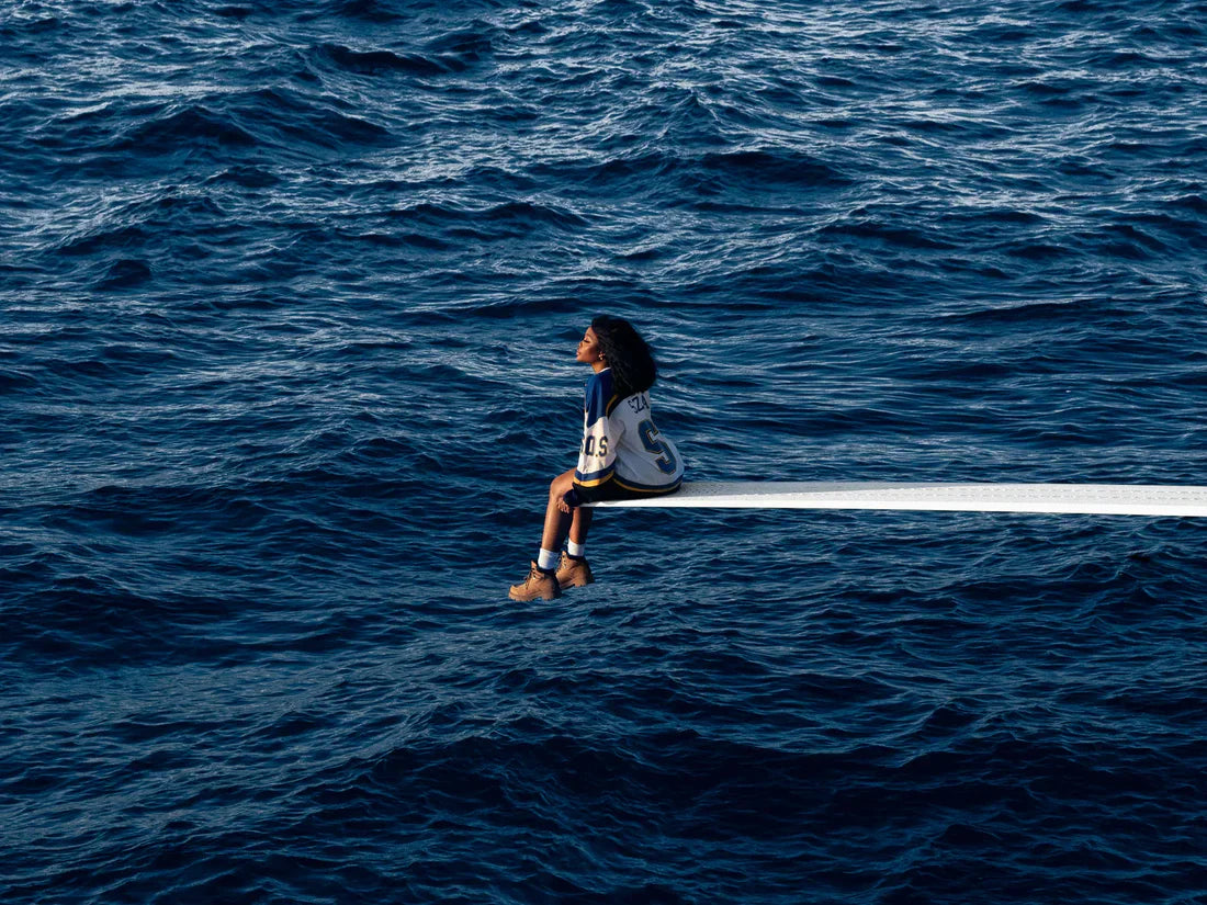 Person wearing sweatshirt with 'SZA' and '5', blue and white, seated by water