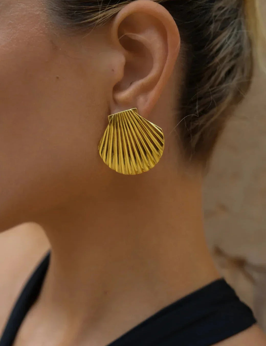Gold shell-shaped earrings on ear close-up