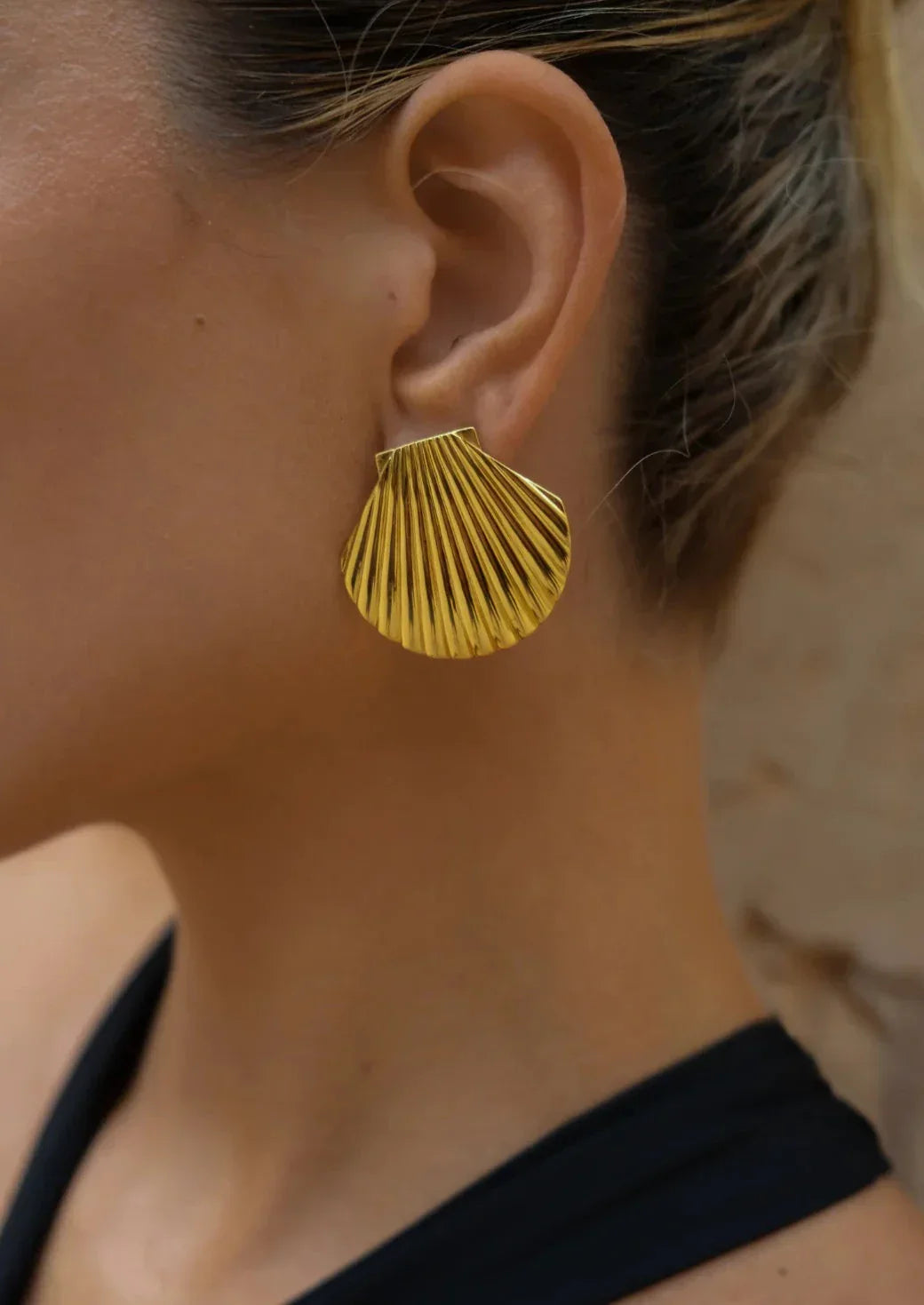 Gold shell-shaped earrings on ear close-up