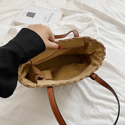 Woven straw tote bag with brown leather handles, interior view with hand