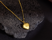 Gold heart pendant necklace on chain displayed on dark stone