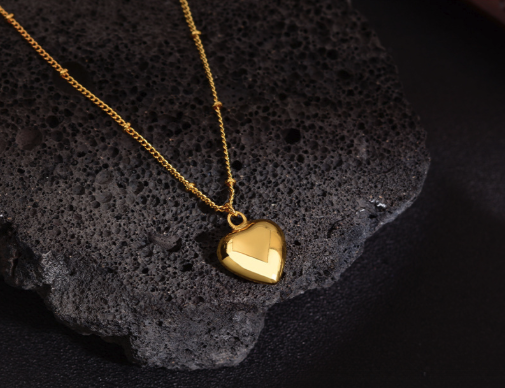 Gold heart pendant necklace on chain displayed on dark stone