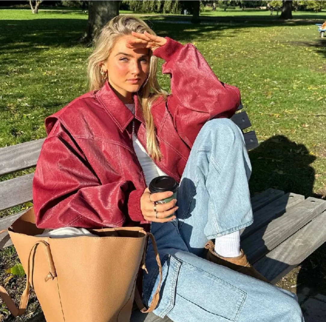 Oversized rode leren jas met capuchon, vrouw zittend op bankje in park