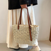 Woven straw tote bag with brown leather handles, front view with model and white skirt