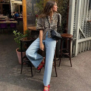 Blouse with leopard print worn with light blue jeans and red shoes, side view