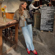 Blouse featuring leopard print worn with light blue jeans and red shoes, three-quarter view