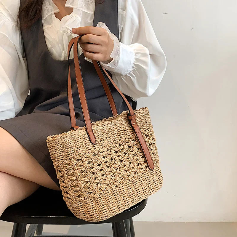 Woven straw tote bag with brown leather handles, front view held by model