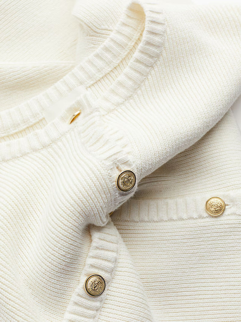 Close-up of white knitted dress with gold buttons
