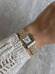 Gold wristwatch with Roman numerals and guilloche dial, worn on wrist with white lace sleeve