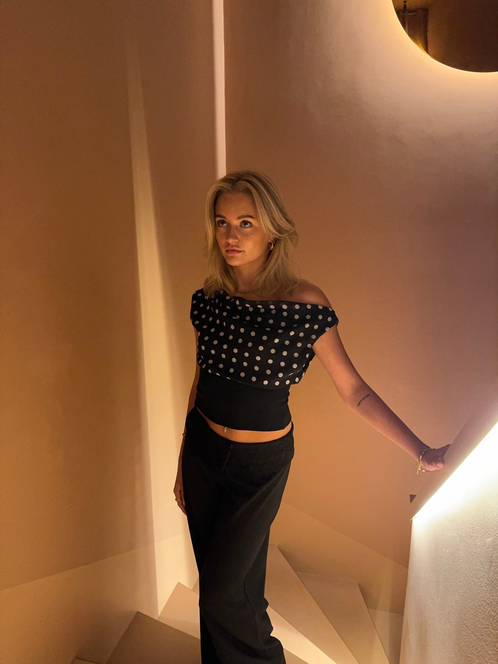 Black top with white polka dots and asymmetrical sleeve three-quarter view