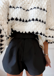 Cream chunky knit sweater with black heart pattern, worn with black shorts, side view