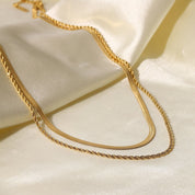 Gold-colored layered necklace on fabric background overhead view