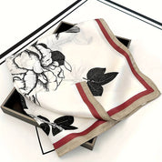 Silk scarf with floral and bird print, red and beige border, folded on black box