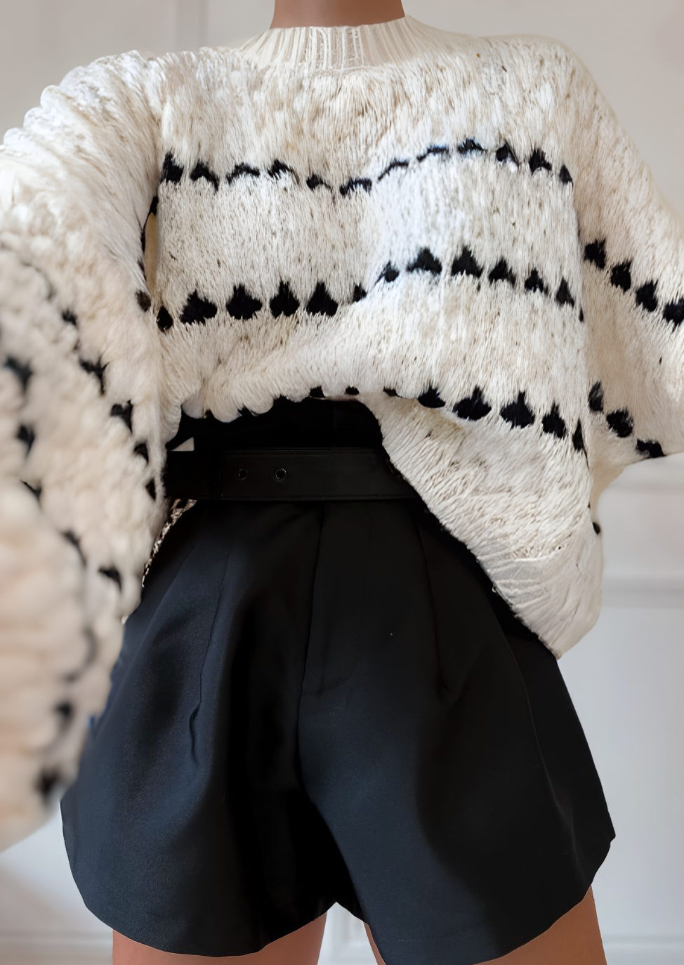 Cream chunky knit sweater with black heart pattern, worn with black shorts, front view with hand on waist