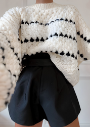 Cream chunky knit sweater with black heart pattern, worn with black shorts, front view with hand on waist