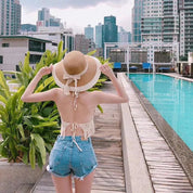Person wearing cream crochet halter top with tassels, back view near pool