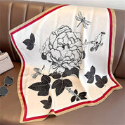 Silk scarf with floral and bird print, red and beige border, laid flat on leather surface