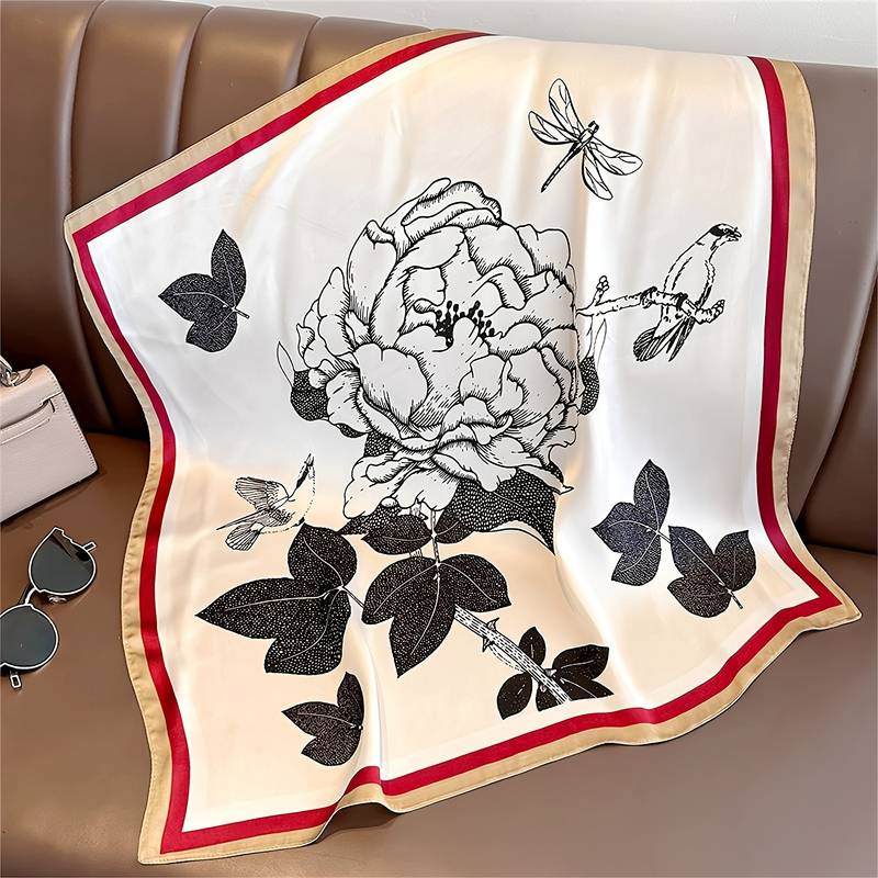 Silk scarf with floral and bird print, red and beige border, laid flat on leather surface