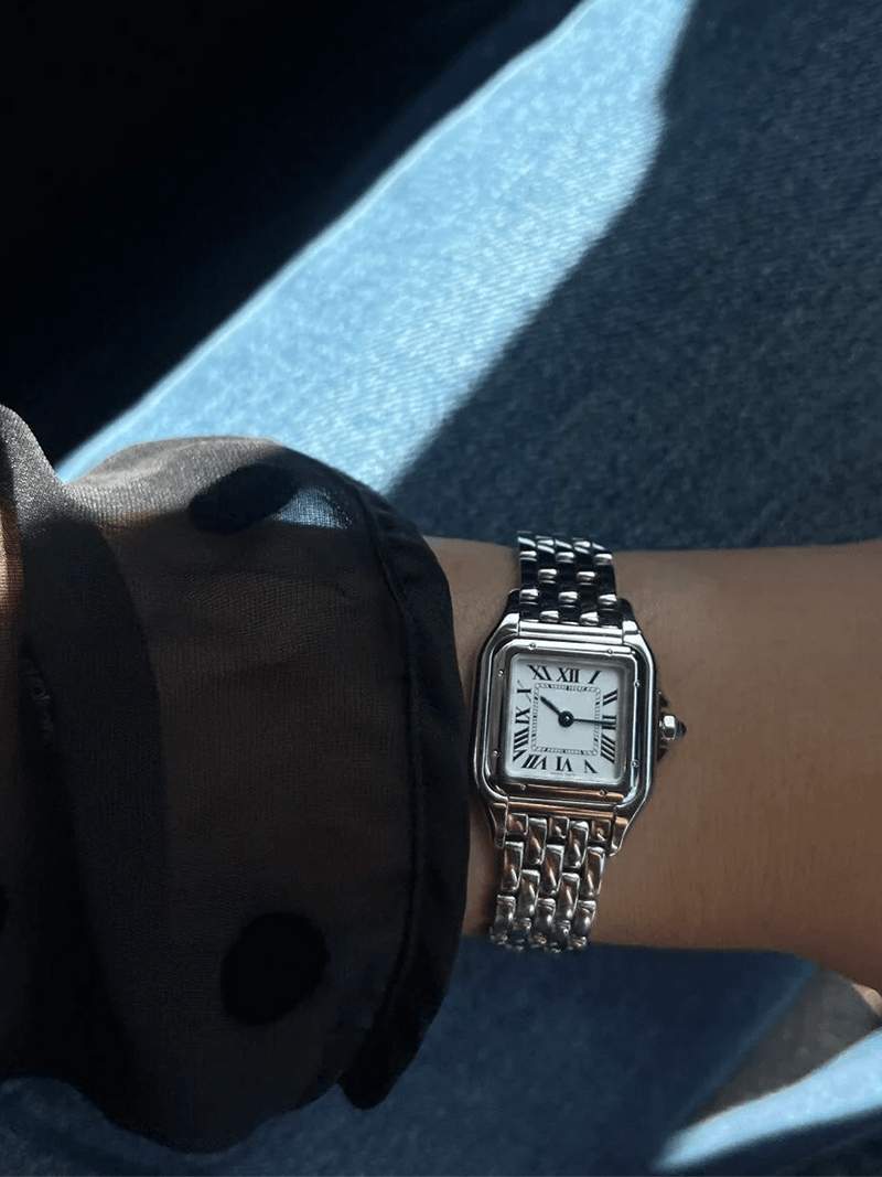 Silver wristwatch with Roman numerals and guilloche dial, worn on wrist with black sleeve