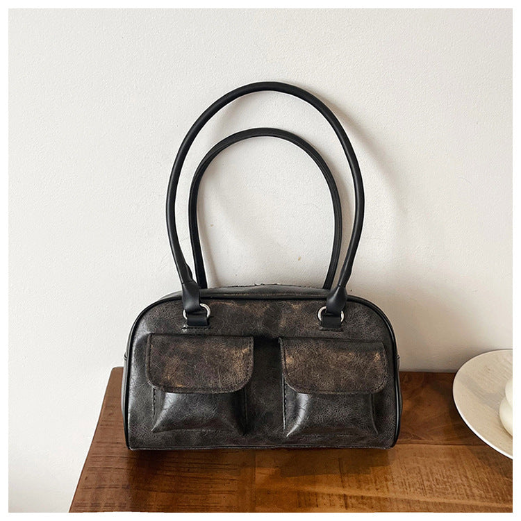 Black leather shoulder bag with front pockets, angled view on wooden surface