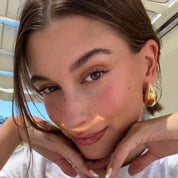 Gold sculptural hoop earrings worn on ear, side view