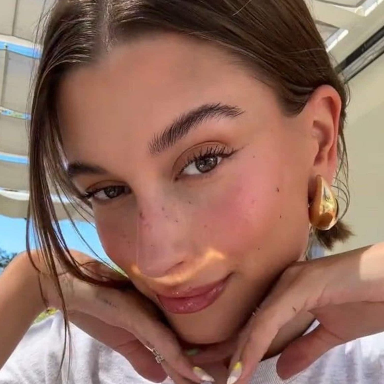 Gold sculptural hoop earrings worn on ear, side view