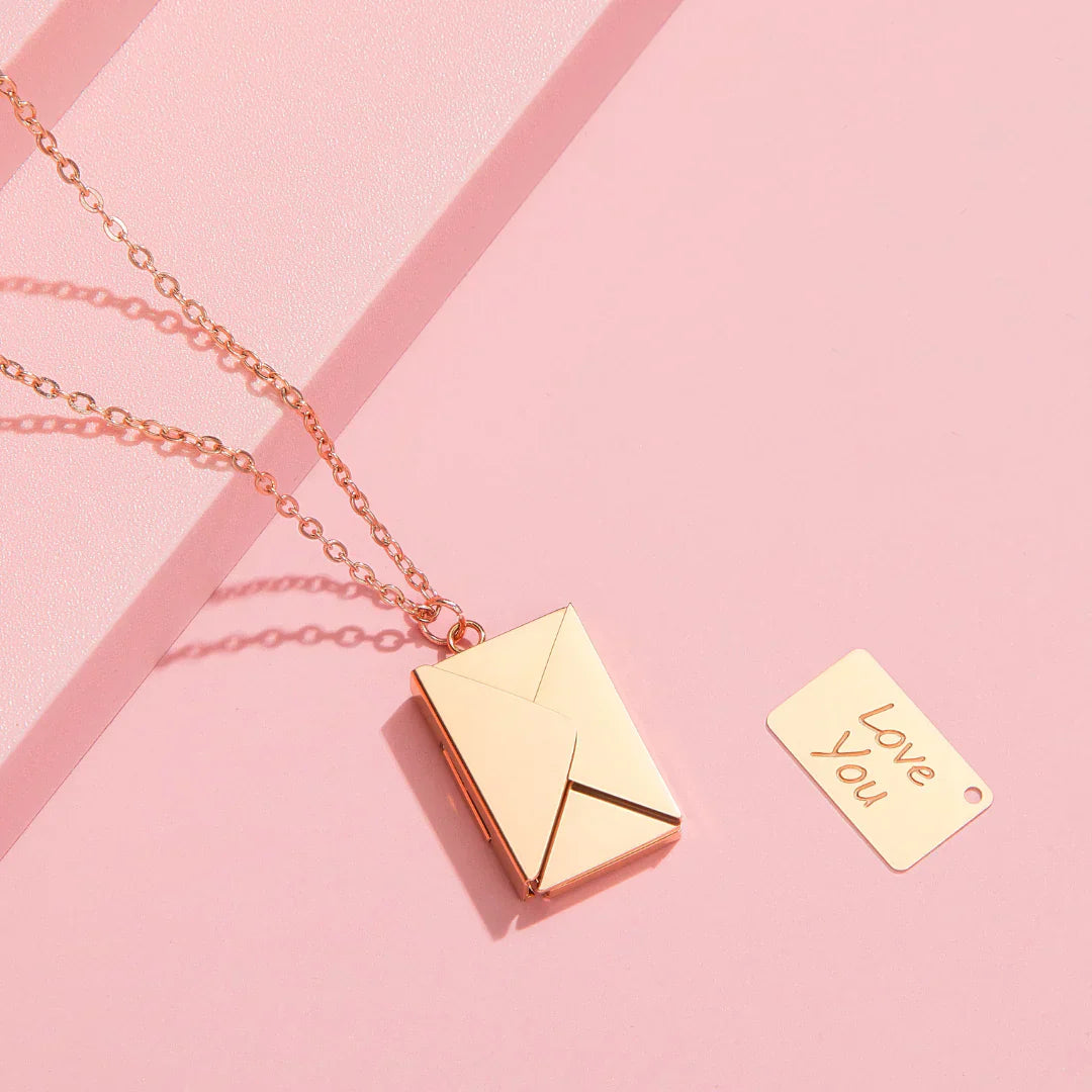Rose gold envelope locket necklace with 'Love You' tag on pink background
