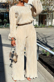 Beige pleated jumpsuit with wide legs and chain strap bag, front view