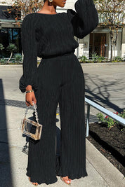 Black pleated jumpsuit with wide legs and chain strap bag, front view