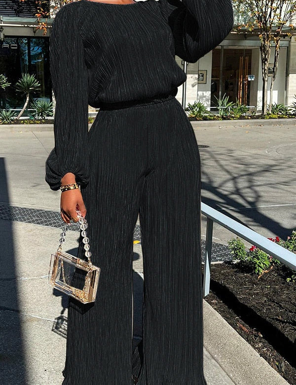 Black pleated jumpsuit with wide legs and chain strap bag, front view