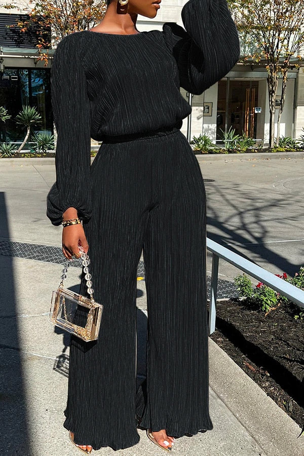 Black pleated jumpsuit with wide legs and chain strap bag, front view