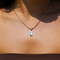 Gold necklace with teardrop-shaped green stone pendant, worn on neck