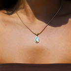 Gold necklace with teardrop-shaped green stone pendant, worn on neck