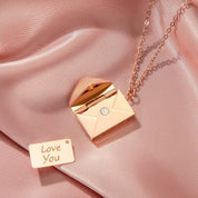 Rose gold envelope locket necklace on satin fabric with 'Love You' tag